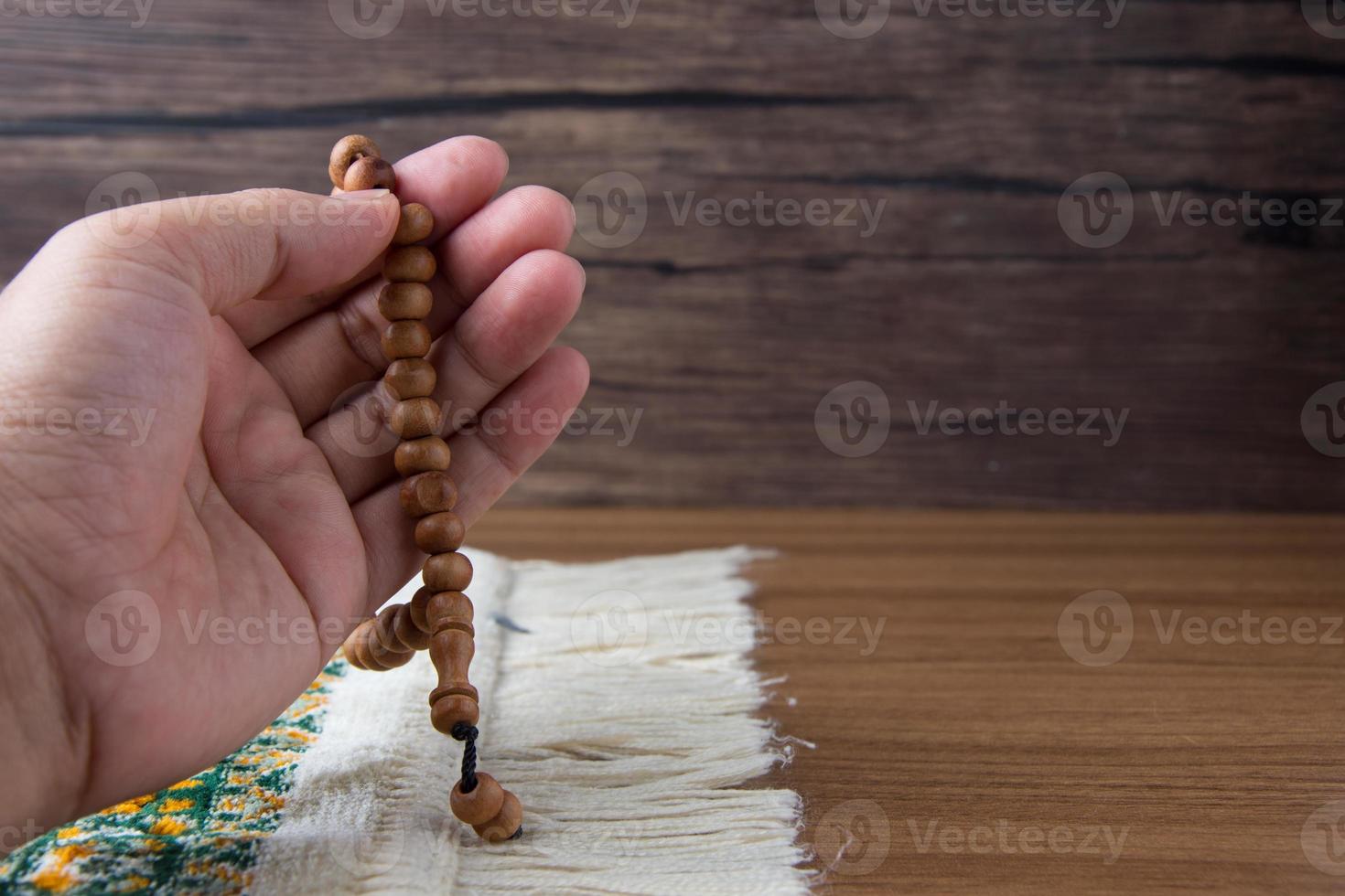 Orando, palmas arriba cuando Orando en islámico cultura, que lleva oración rosario en un oración alfombra en un de madera antecedentes y allí es luz solar, vacío espacio, Copiar espacio, foto