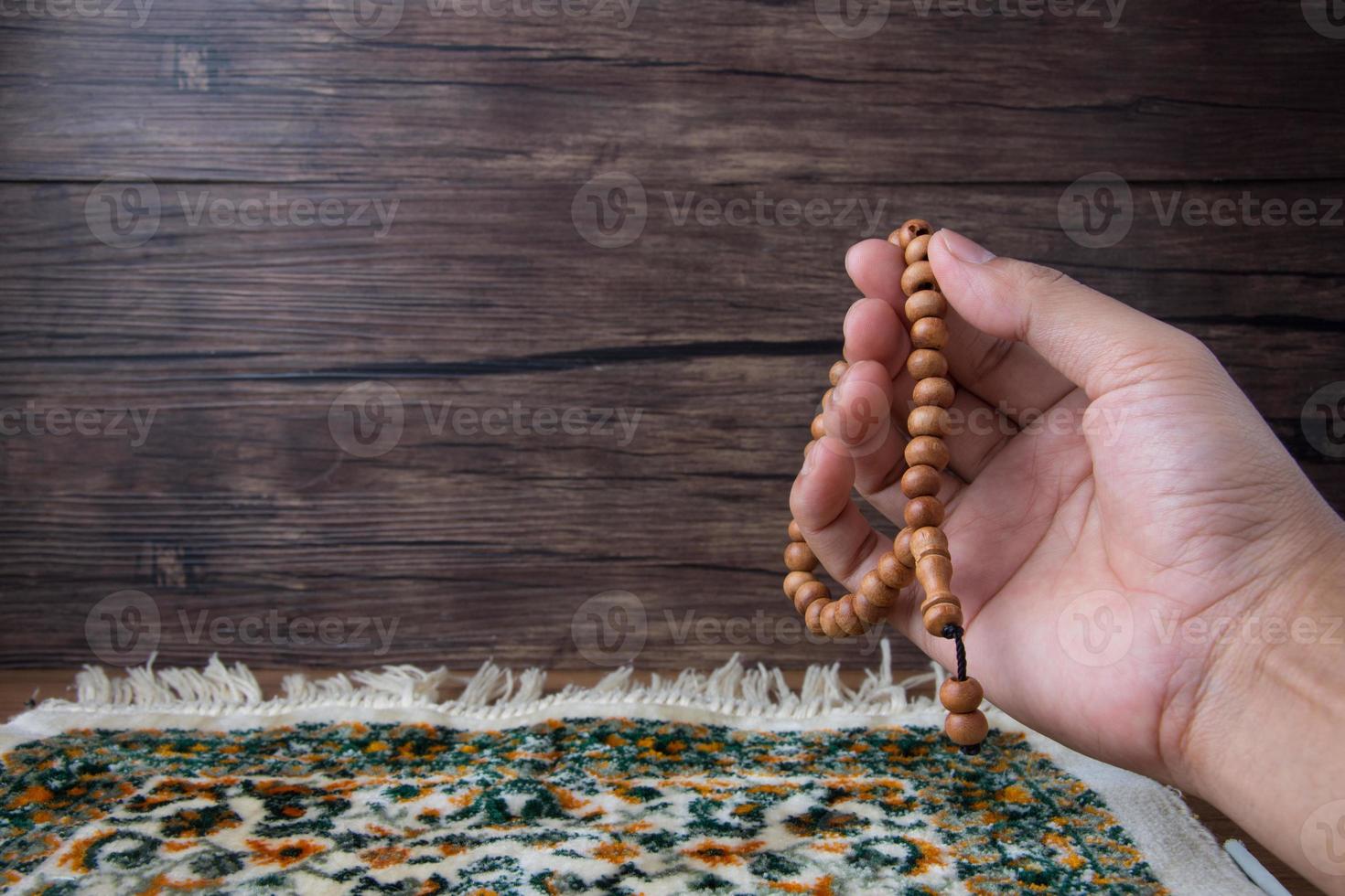 praying, palms up when praying in Islamic culture, carrying prayer beads on a prayer rug on a wooden background and there is sunshine, empty space, copy space, photo