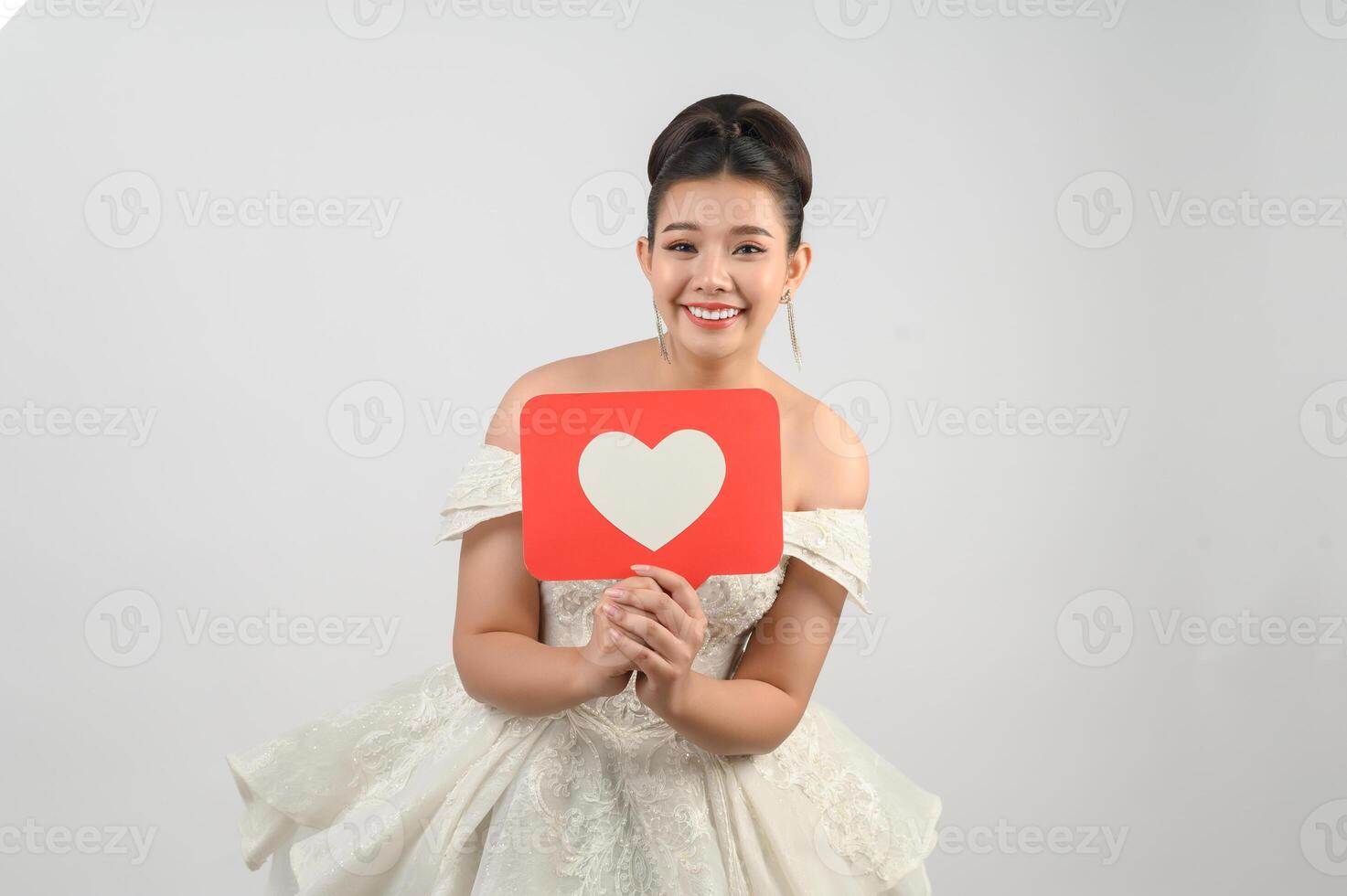 Asian beautiful bride smiling and posing with heart sign on white background photo