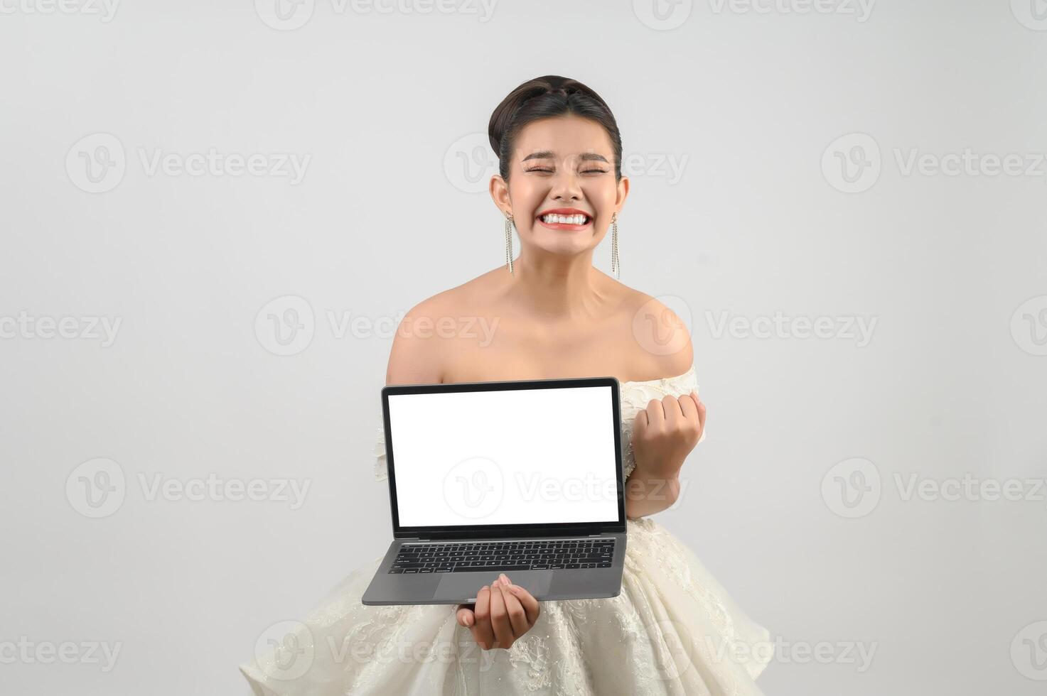 Una joven novia asiática hermosa posa con una computadora portátil de maqueta en la mano foto