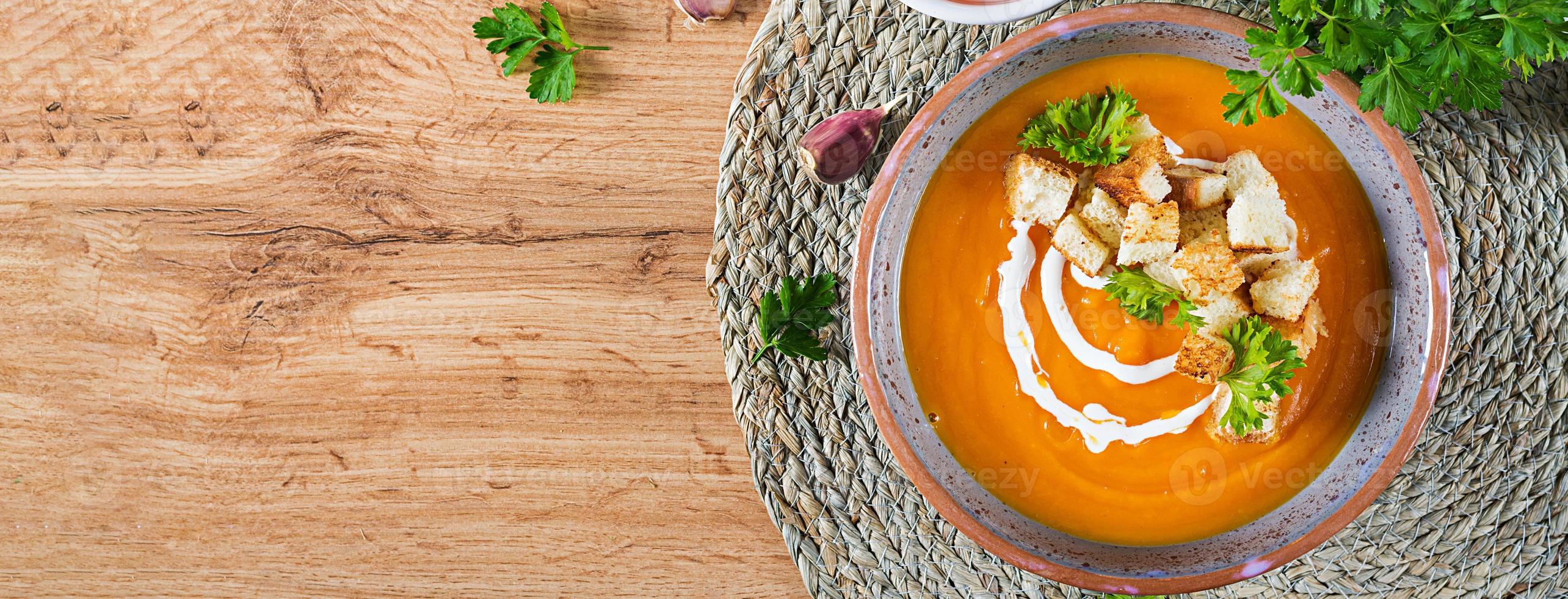 Pumpkin soup in a bowl served with parsley and croutons. Vegan soup. Thanksgiving day food. Halloween meal. Banner. Top view photo