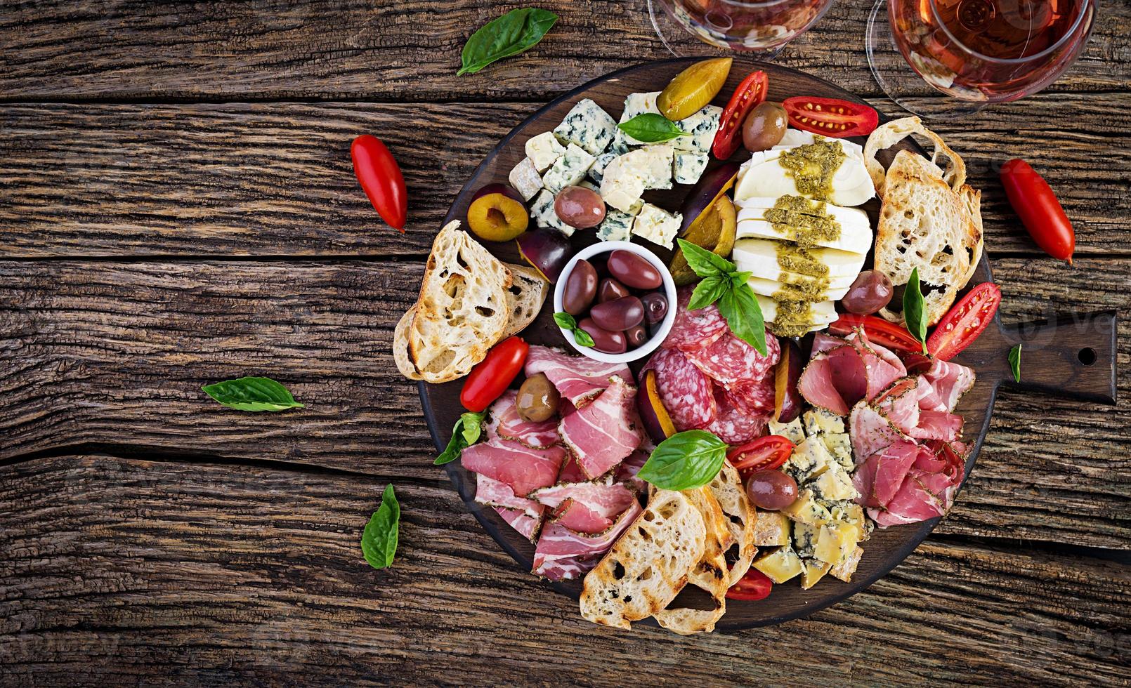 Antipasto platter with ham, prosciutto, salami, blue cheese, mozzarella with pesto and olives on a wooden background. Top view, overhead photo