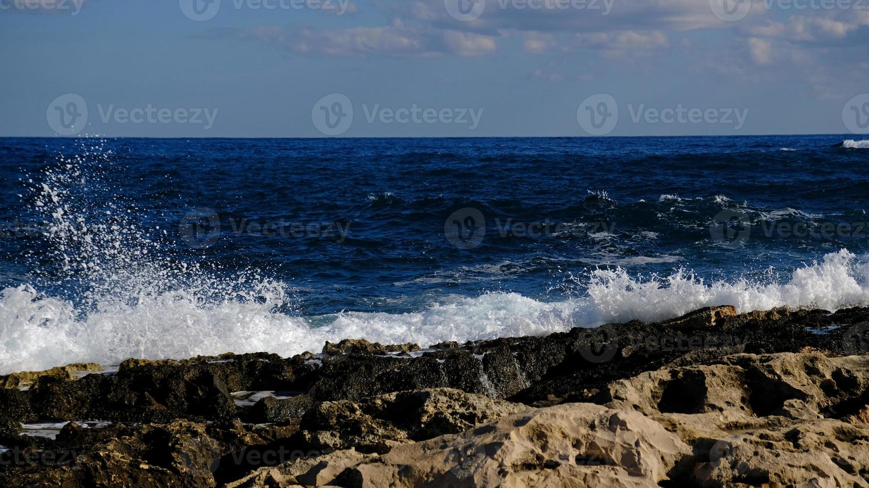 Blue sea wave and white foam and splash. Stone beach on island of Malta, no sandy beach. Summer holiday border frame concept. Tropical island vacation backdrop. Tourist travel banner design template. photo