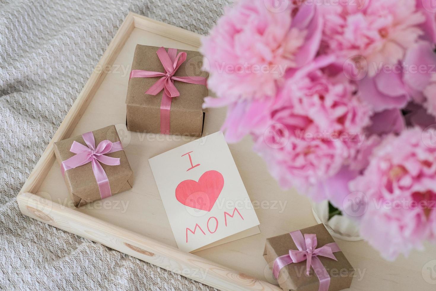 A bouquet of peonies and a card with the text I love mom on a tray. Mother's day concept photo