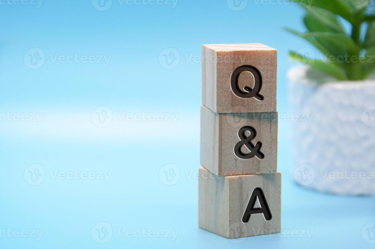 Q and A text engraved on wooden blocks with light blue and table plant background. Question and answer concept. Copy space photo