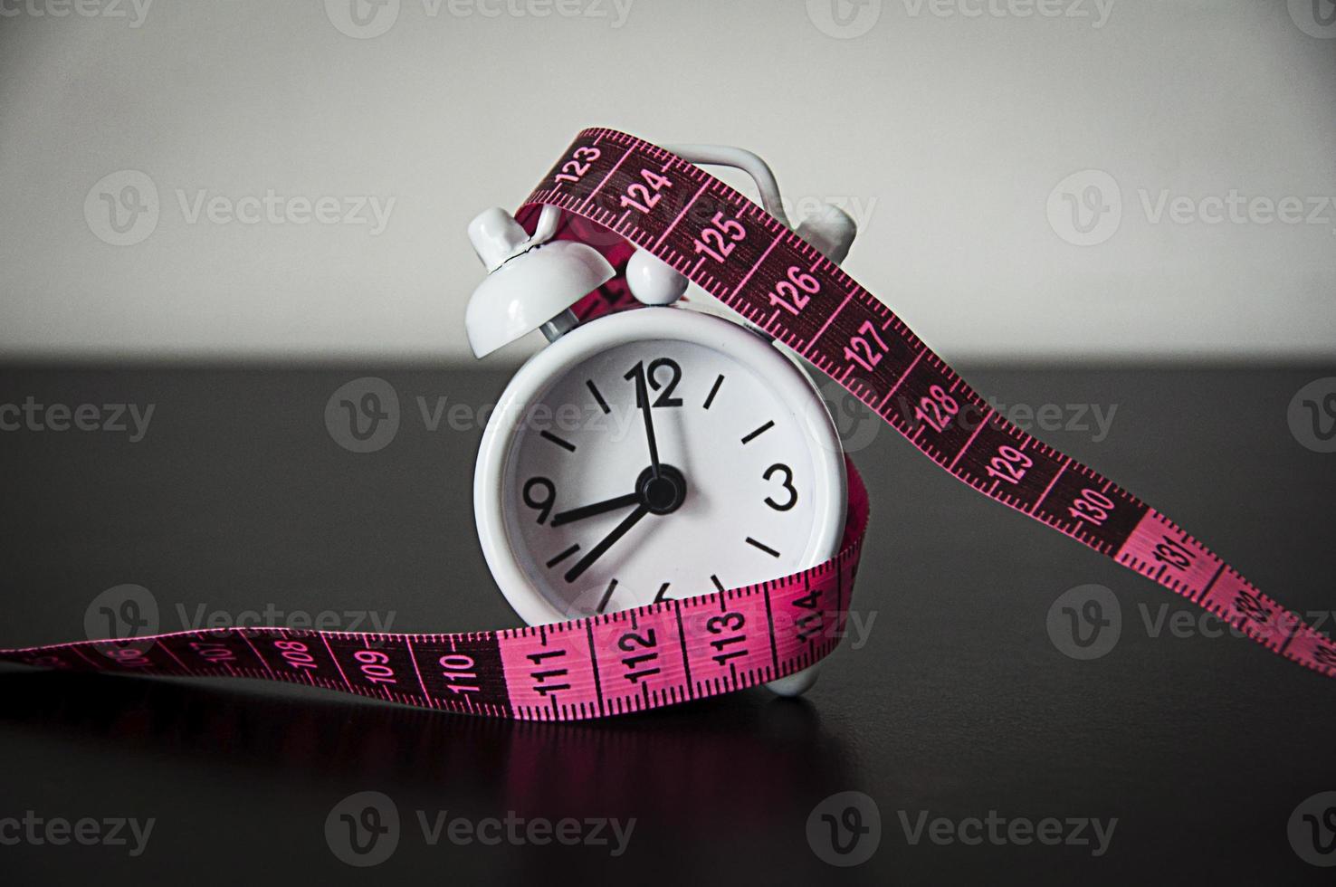 White alarm clock wrapped with measuring tape background. photo