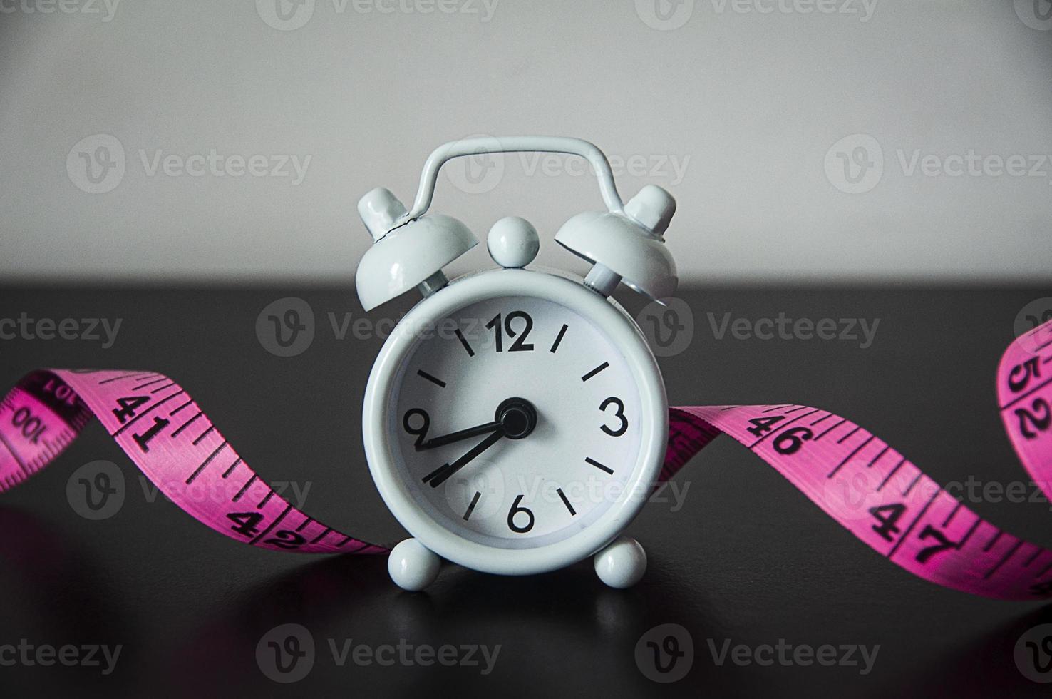 White alarm clock with measuring tape background. photo