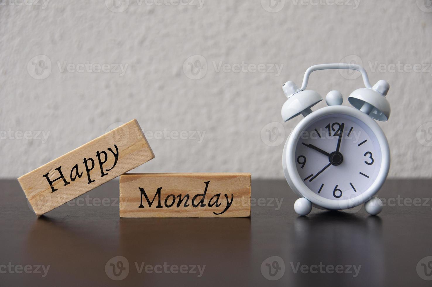 Happy Monday text on wooden blocks with white alarm clock background. photo