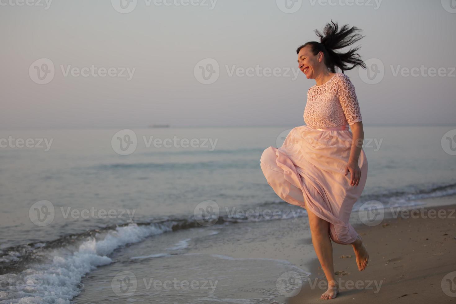 A beautiful middle-aged woman in a dress runs along the seashore. photo