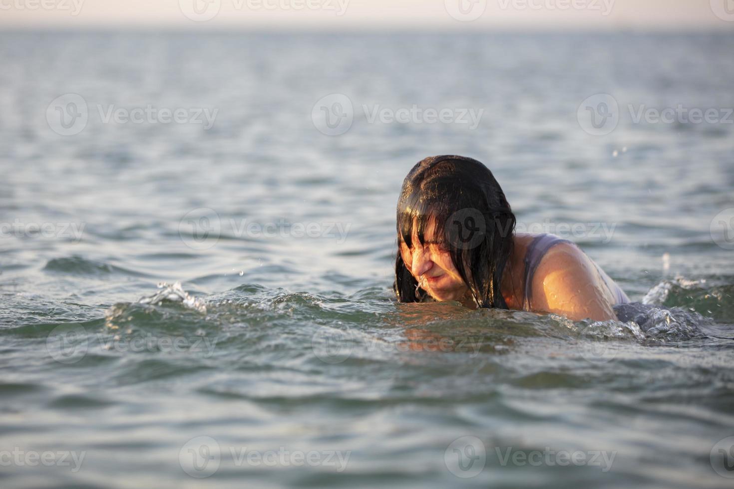 An elderly amusing woman of middle age bathes in the sea. Funny face of a woman at the sea. Unsuccessful vacation photo. photo