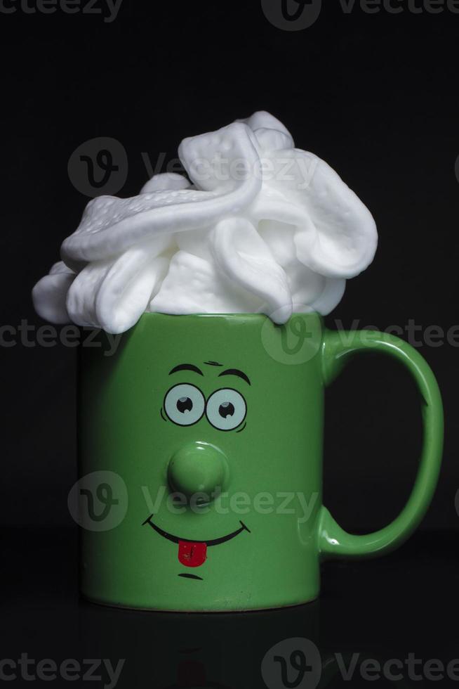 Funny green cup with a cheerful face with whipped cream. An invigorating drink in the morning. photo