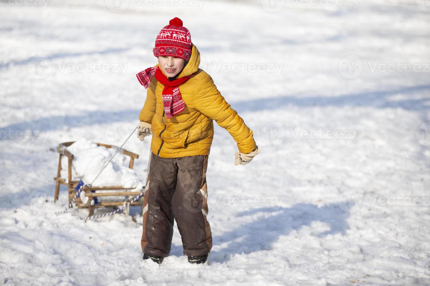 un pequeño gracioso chico paseos en un de madera trineo en el pueblo en un invierno día. foto