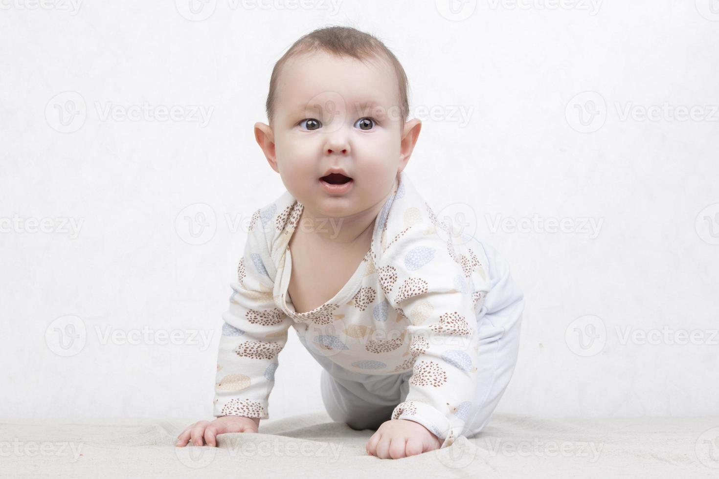 Kid with a smile on a white background. An adorable six month old baby crawls on the bed. Conceptual photo of fatherhood and motherhood.