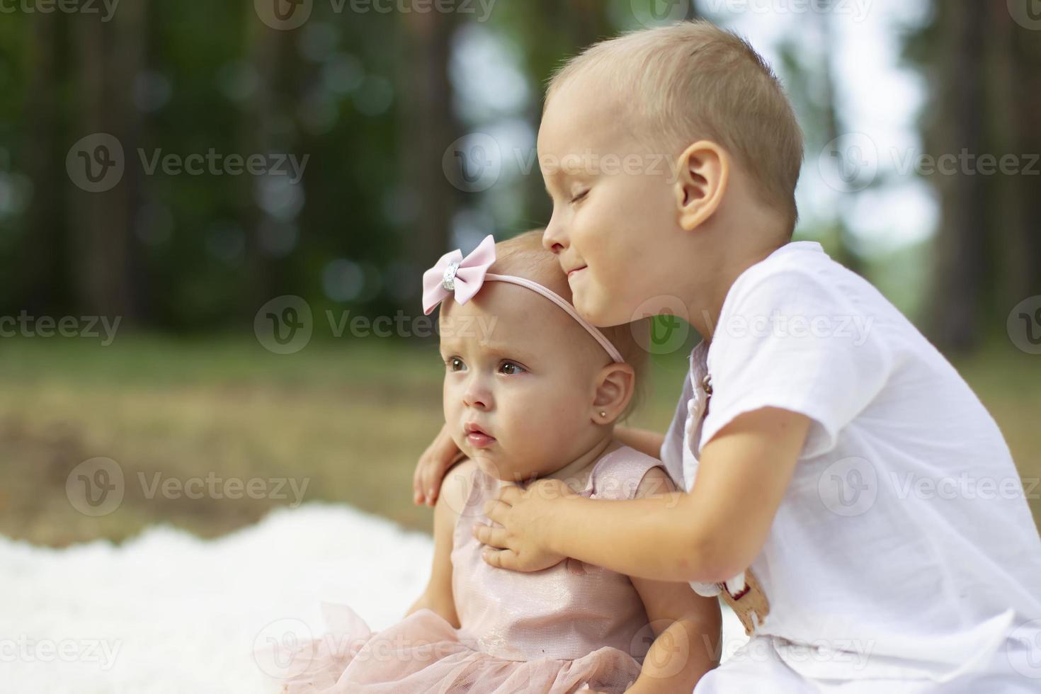 The older brother hugs his little sister for a walk in the park. photo