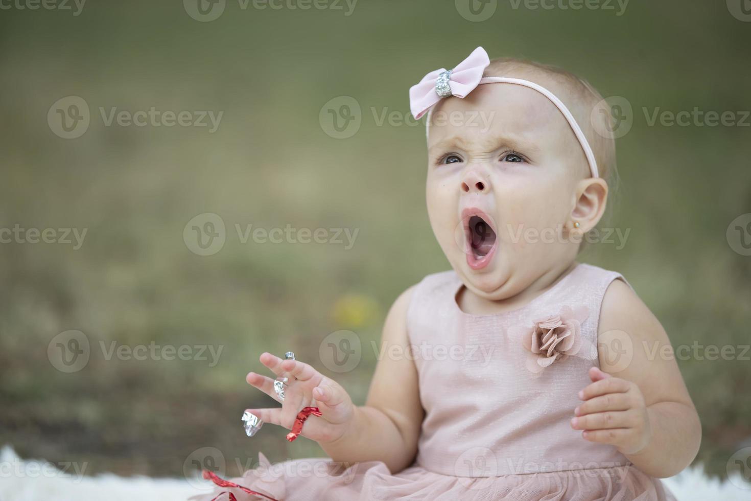 Funny little girl yawns on a summer walk. The child is one year old. photo