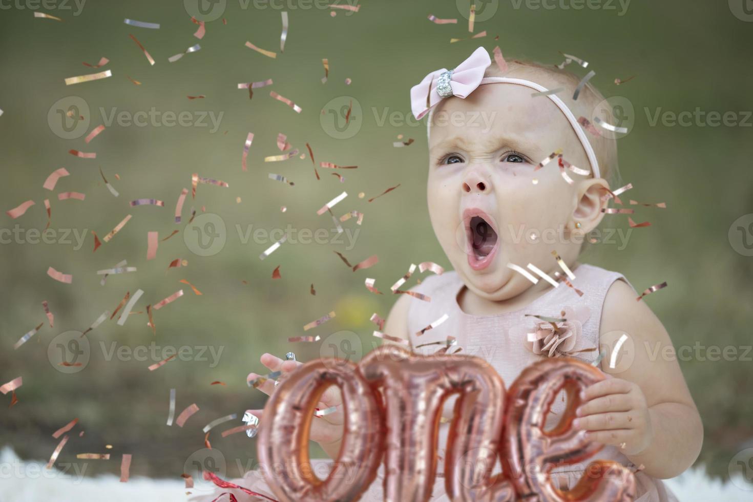 A funny little girl in a bright confetti yawns. Bored child at the birthday party. Beautiful baby. photo