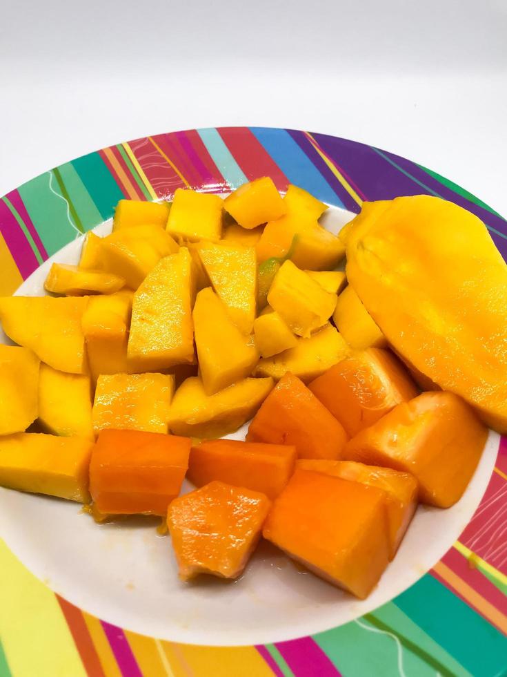 slices of mango and papaya fruit on a colorful motif plate photo