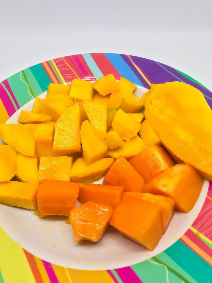 slices of mango and papaya fruit on a colorful motif plate photo