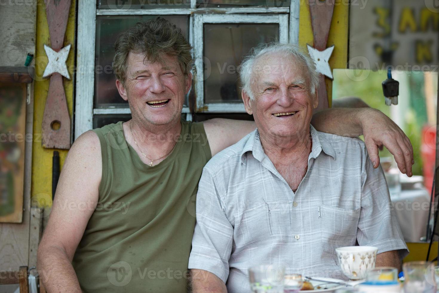 An adult son and an old man father have fun laughing, hugging and looking at the camera. photo