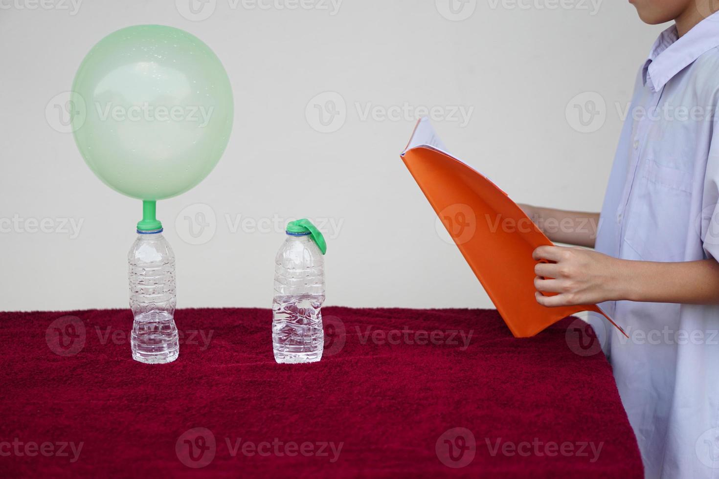 Closeup student study science experiment about reaction of chemical in bottles and balloons. Read  the result of experiment in book. Concept, science subject activity, education. Learning by doing photo