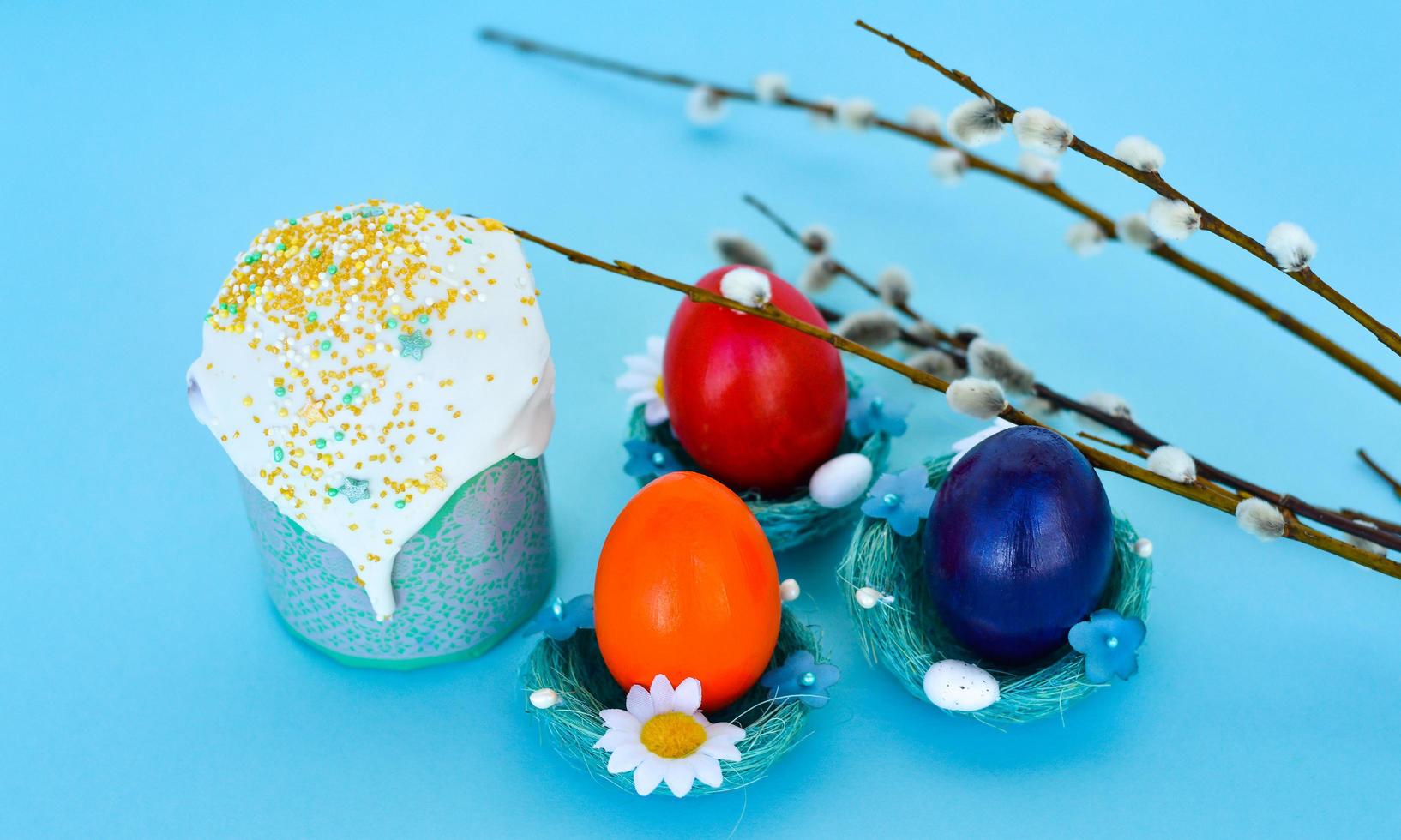 Happy Easter Colorful eggs with cherry blossoms and cake lay on blue background. Spring greeting card photo