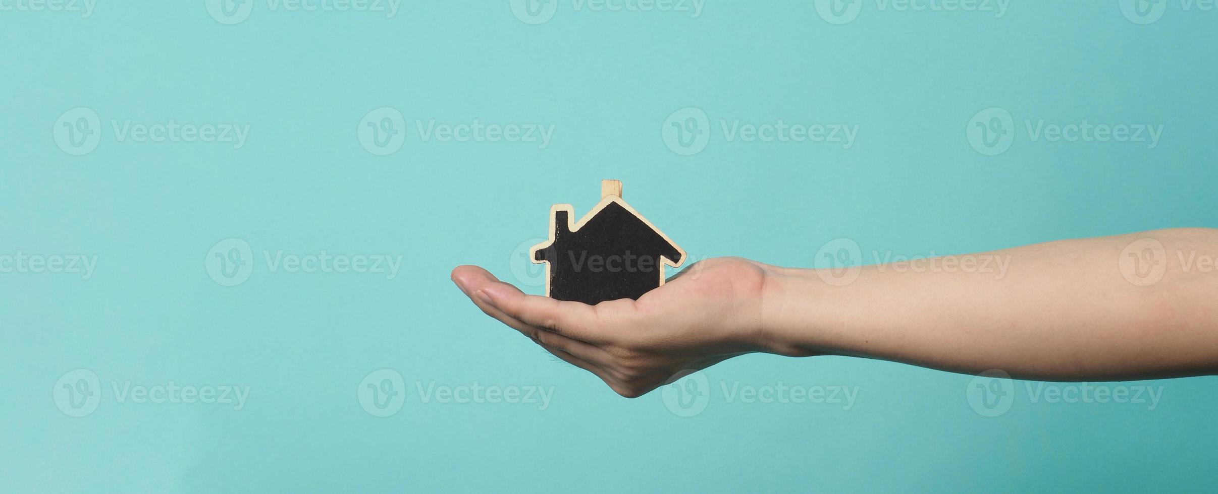 la pequeña casa de madera en las manos representa conceptos como el cuidado del hogar, el amor familiar, la vivienda, el seguro de vivienda y la hipoteca. manos sosteniendo una casa modelo pequeña aislada en el fondo del estudio verde azul. foto