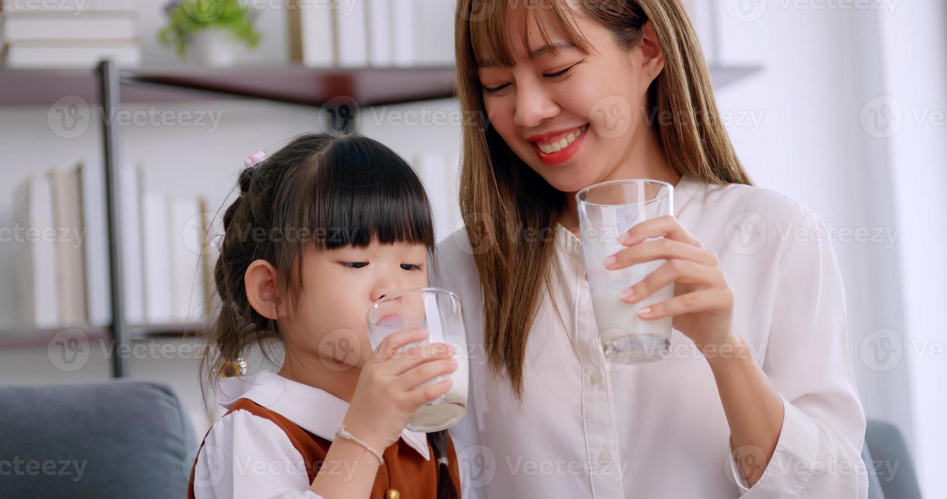 A little girl daughter sitting on sofa, drinking milk with mother in morning. photo