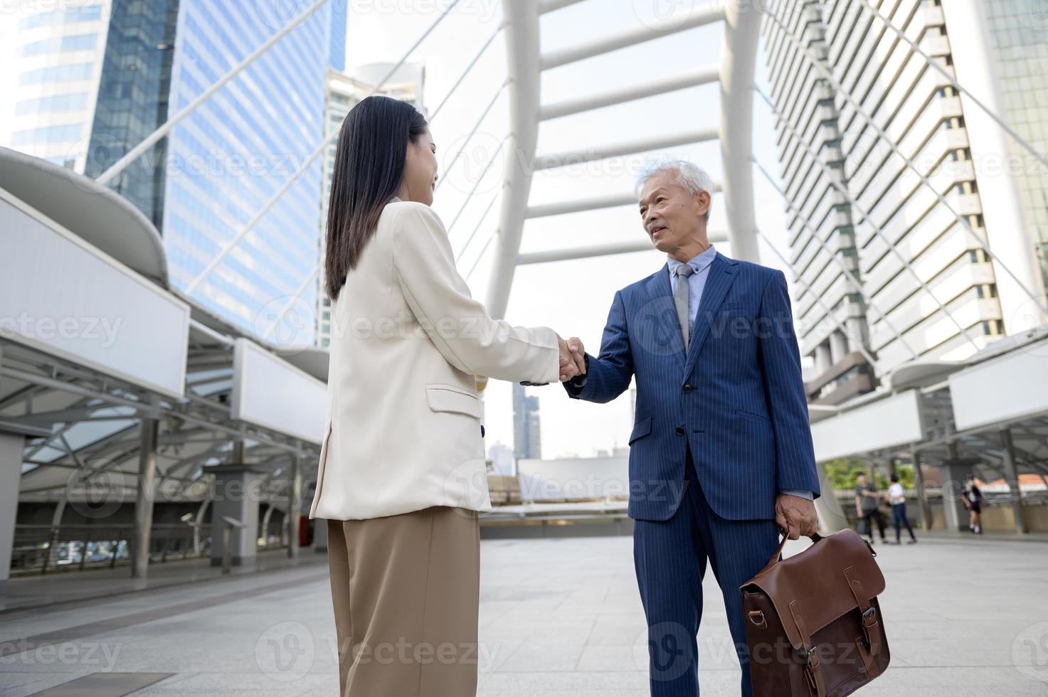 Asian senior mature middle aged businessman handshaking young businesswoman in modern city photo
