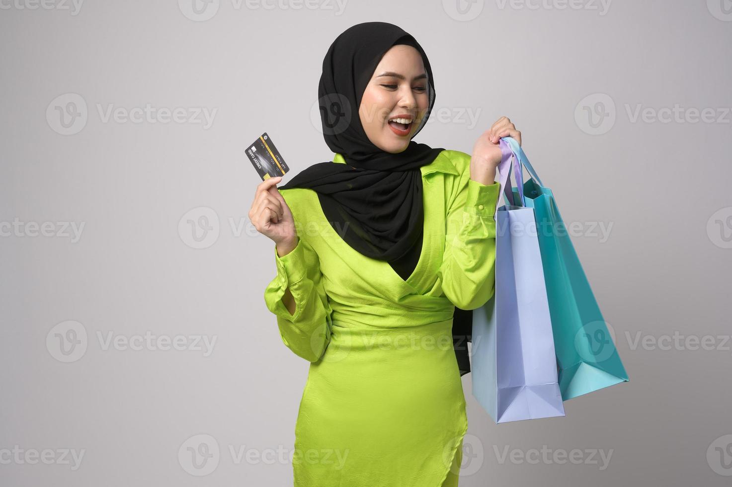 Beautiful musllim woman with hijab holding credit card and shopping bag over white background studio, shopping and finance concept. photo