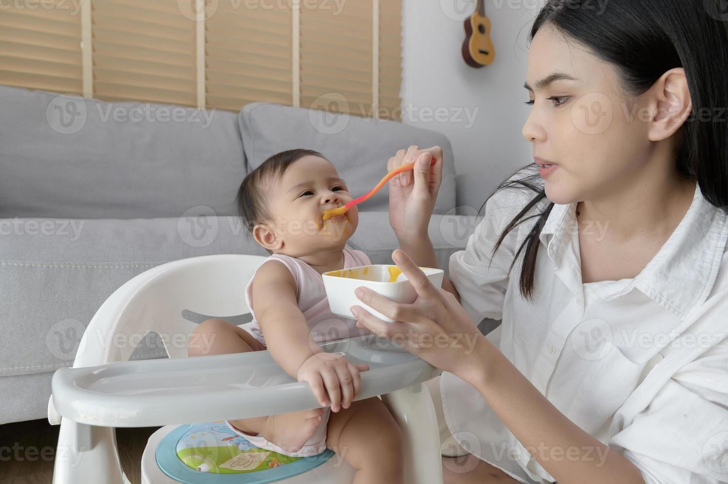 joven madre Ayudar bebé comiendo mezcla comida en bebé silla foto