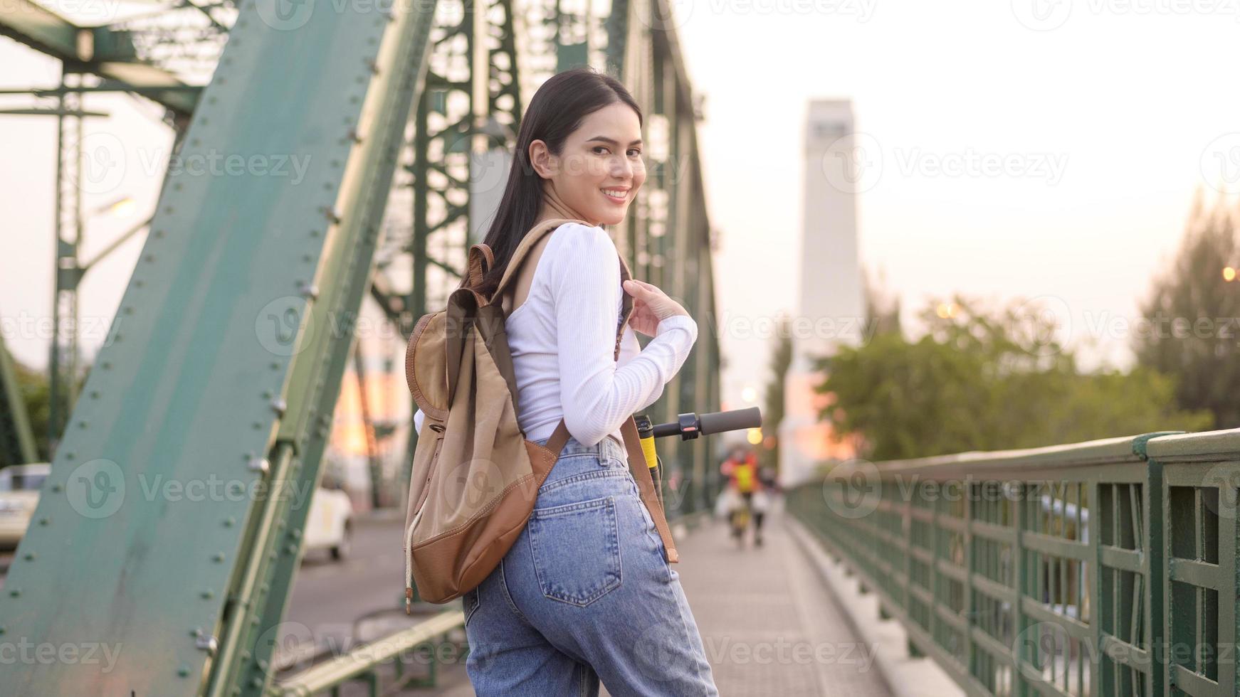 Portrait of young beautiful woman with an electric scooter  over bridge in modern city  background photo