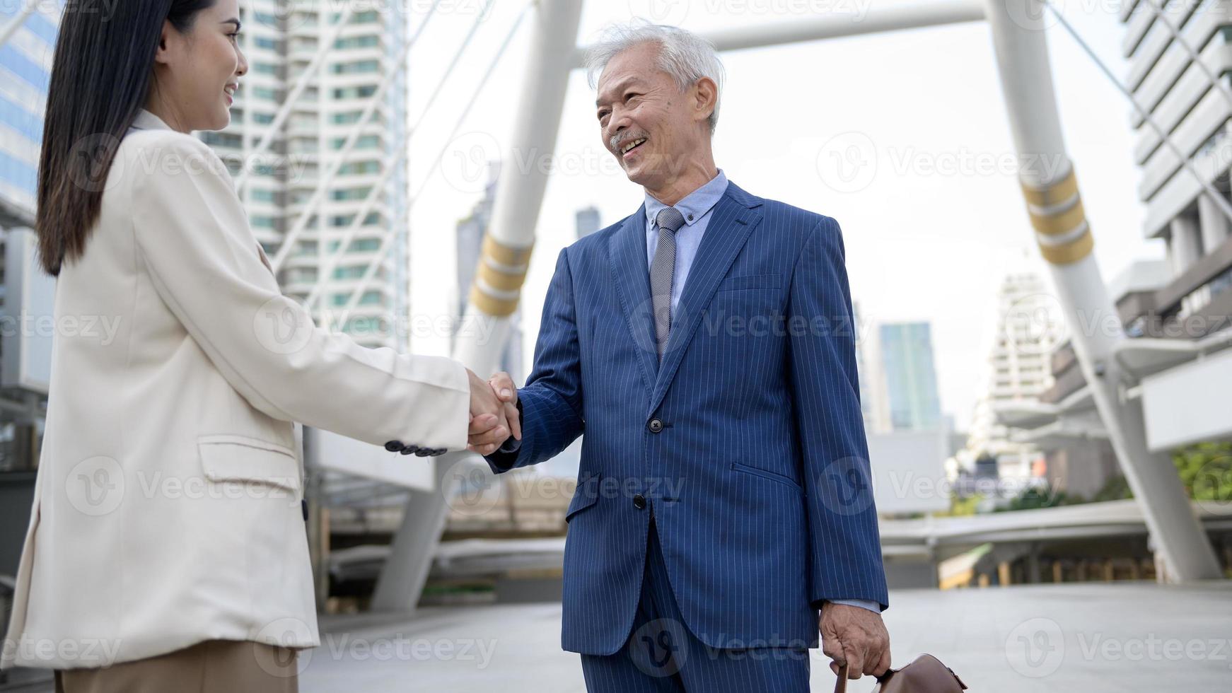 Asian senior mature middle aged businessman handshaking young businesswoman in modern city photo