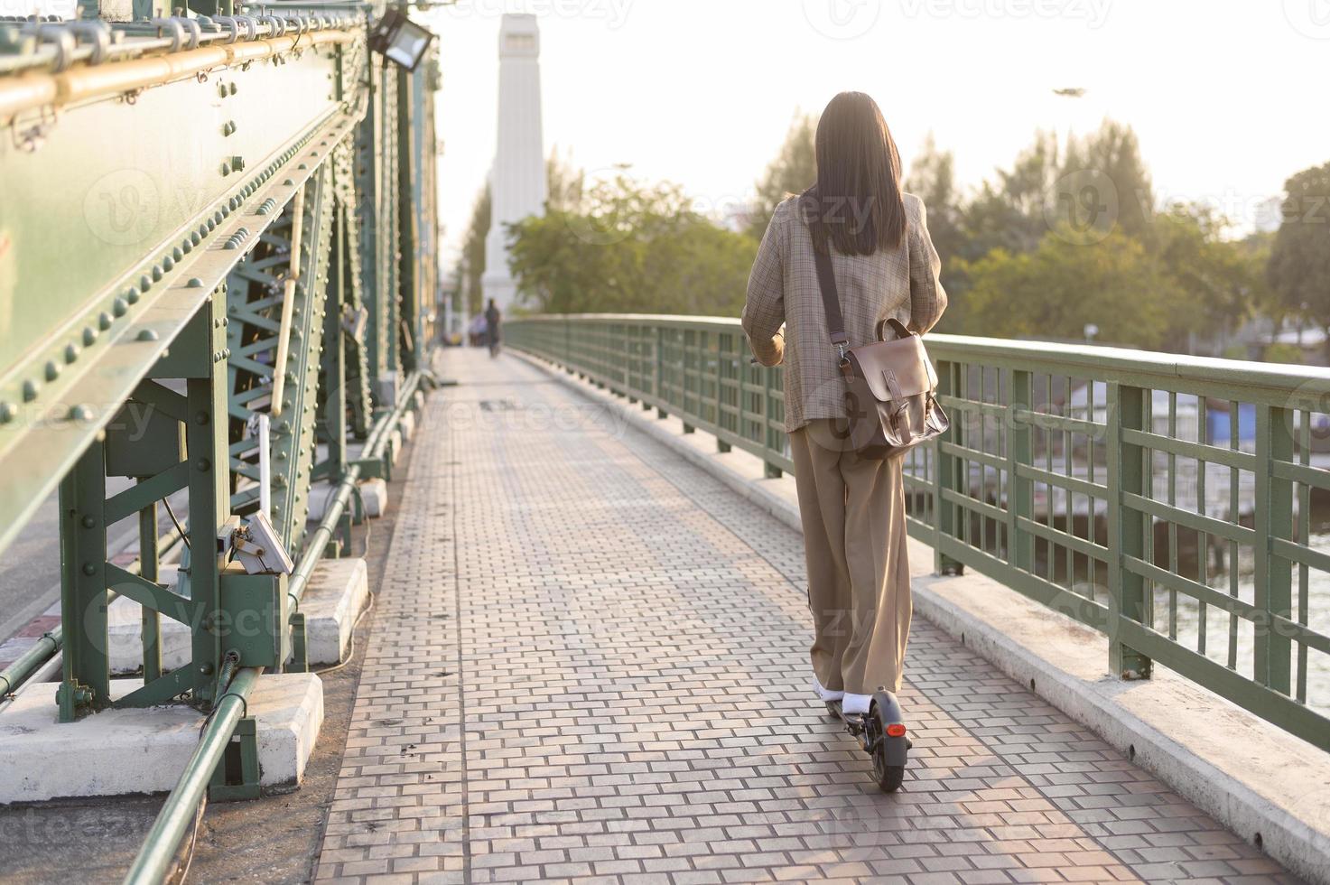 retrato de joven negocio mujer con un eléctrico scooter a trabajo terminado puente en moderno ciudad antecedentes foto