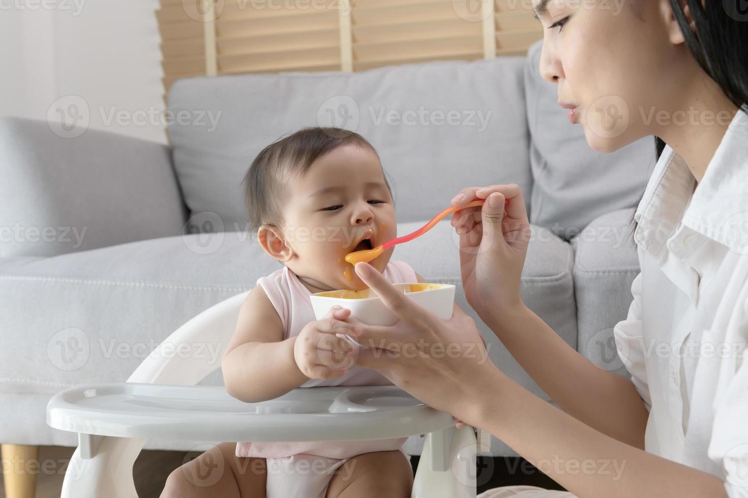 joven madre Ayudar bebé comiendo mezcla comida en bebé silla foto