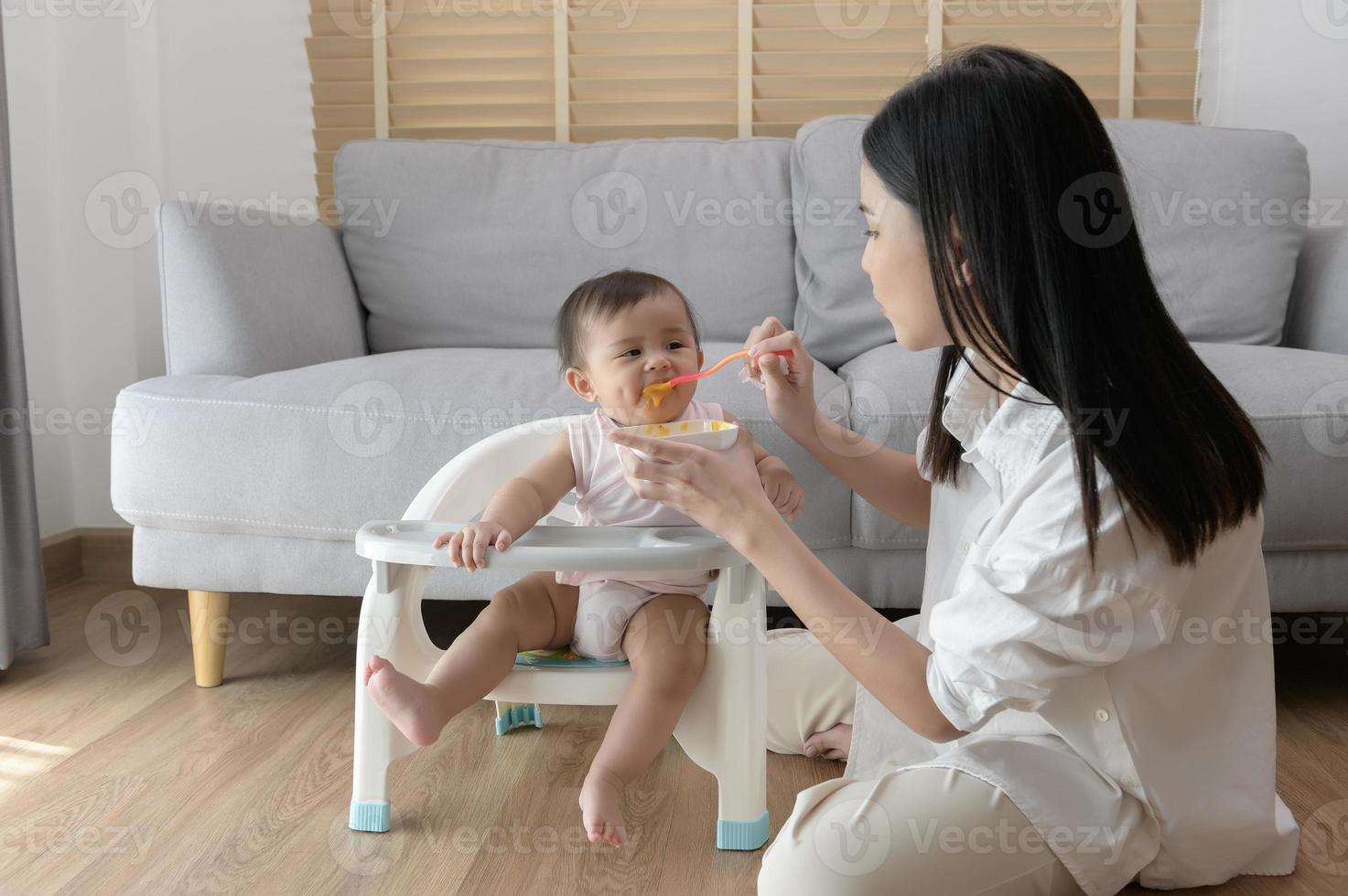 Young mother helping baby eating blend food on baby chair photo