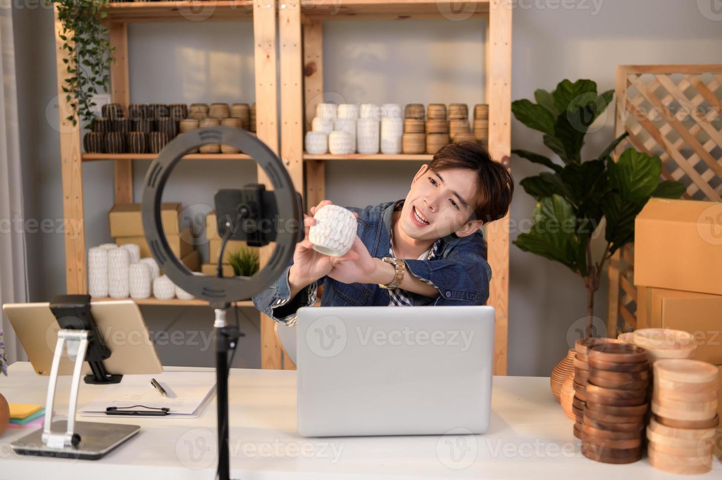 A young Asian man entrepreneur live streaming to sale craft products  to customers in his shop , Technology online business concept. photo