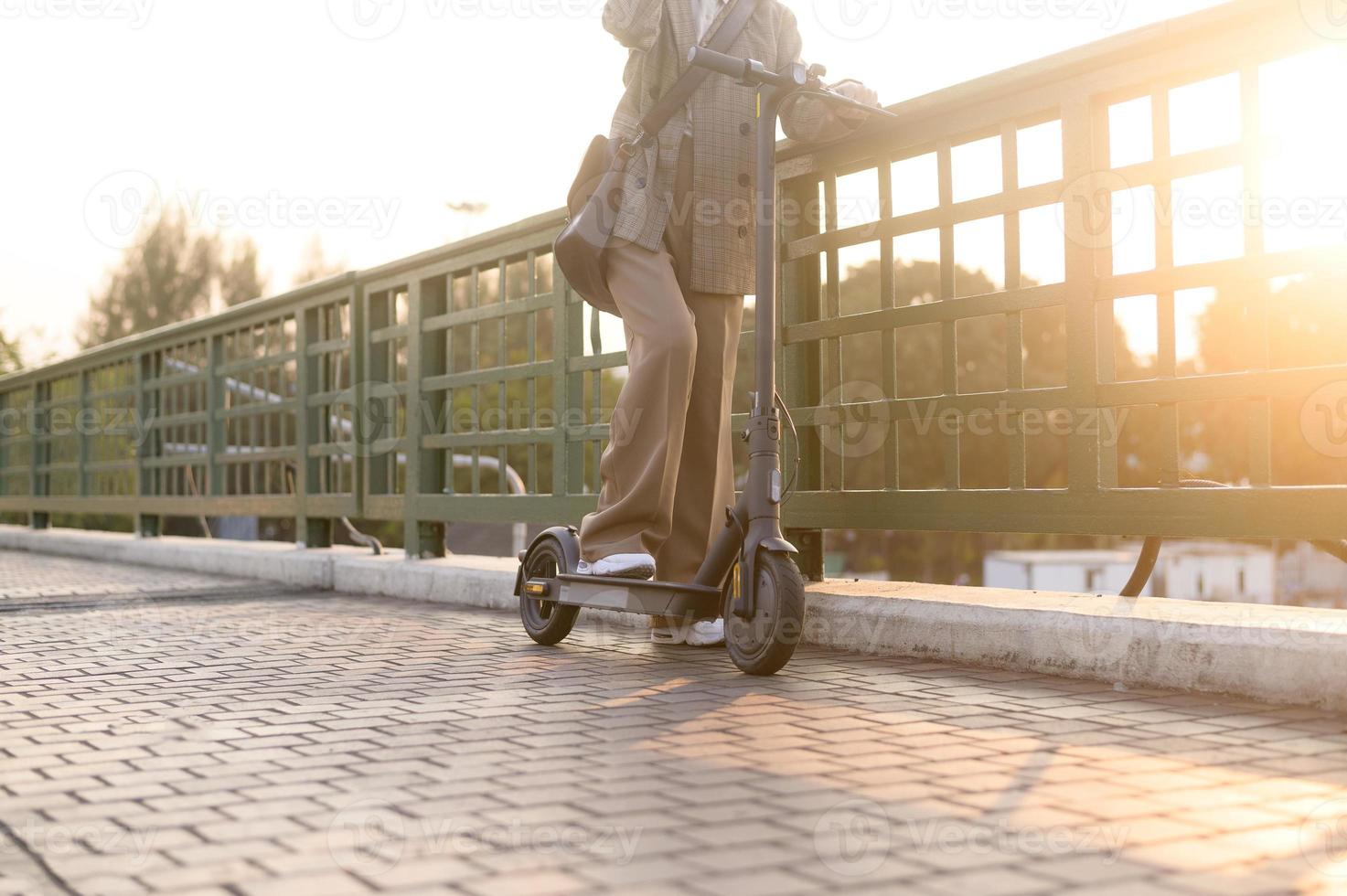 Portrait of young business woman with an electric scooter to work over bridge in modern city  background photo