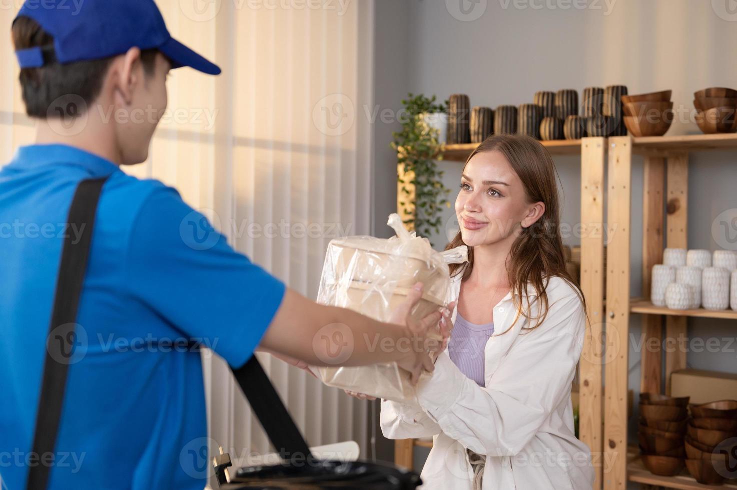 An Asian delivery man wearing blue uniform sending food to young woman customer in her shop photo