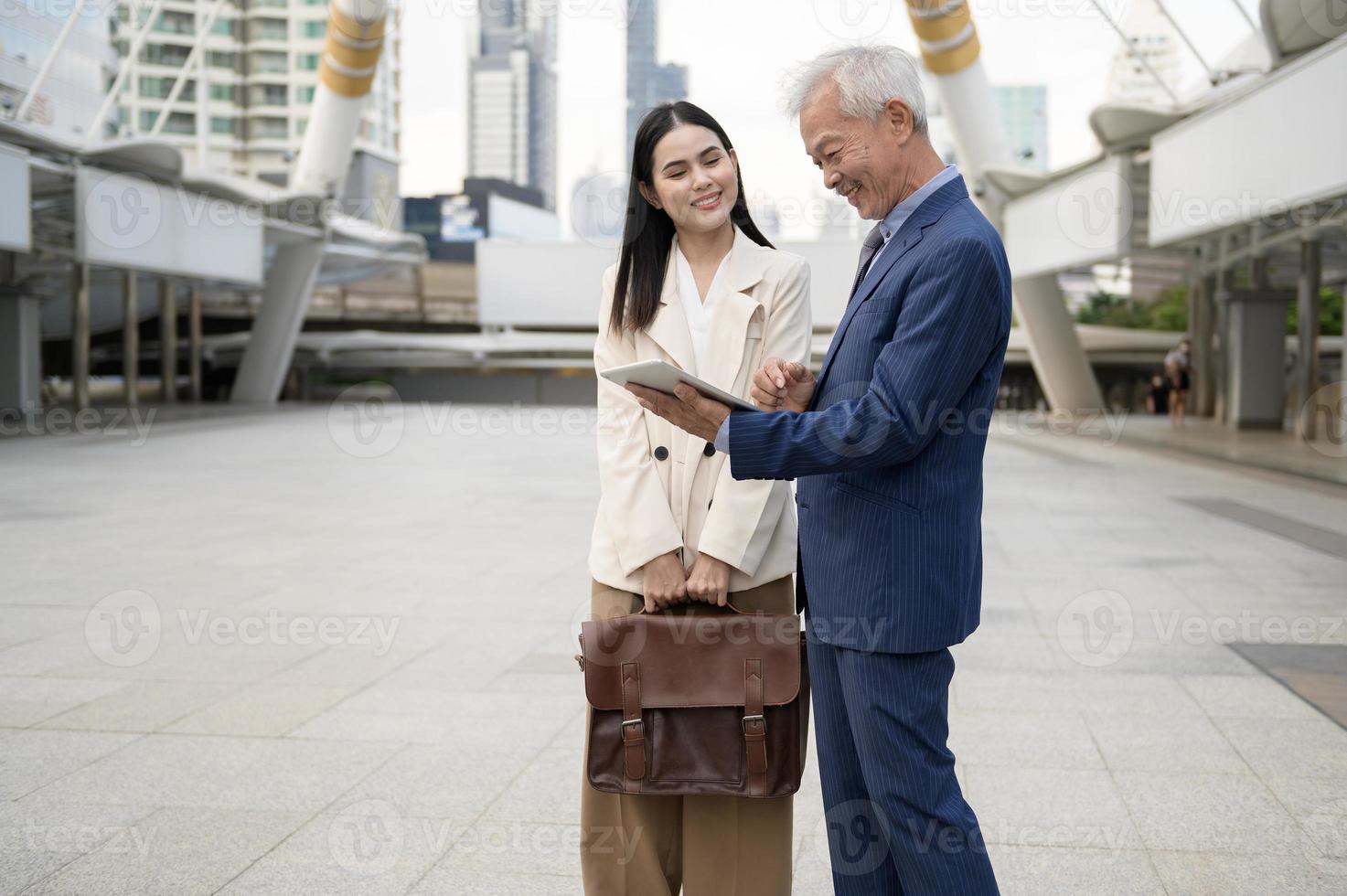 Asian senior mature middle aged businessman and young businesswoman having a discussion and using tablet in modern city photo