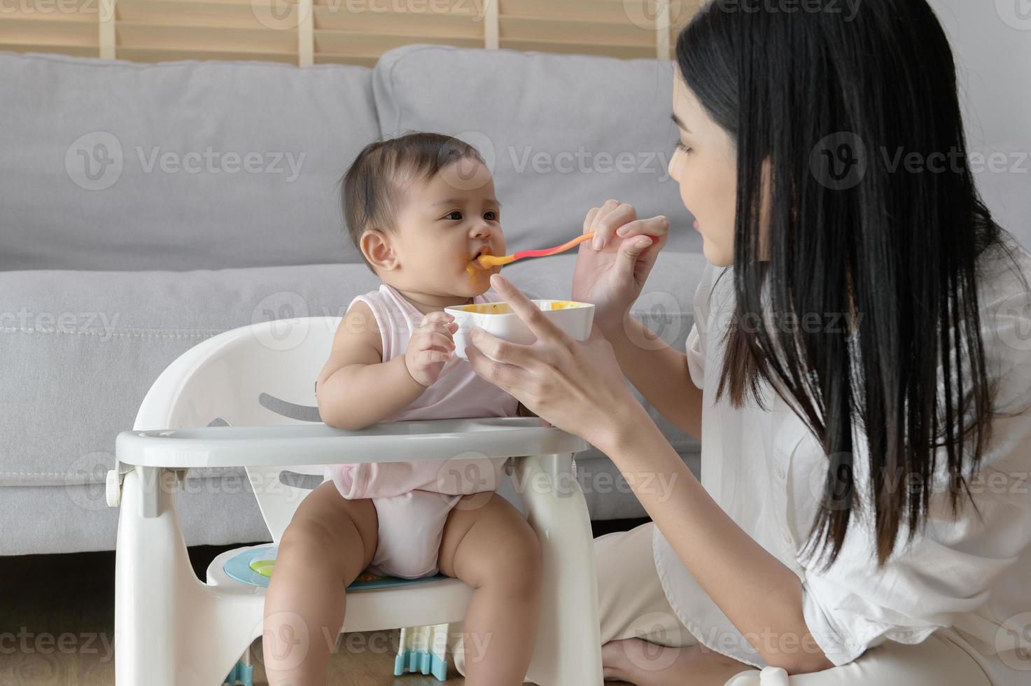 joven madre Ayudar bebé comiendo mezcla comida en bebé silla foto