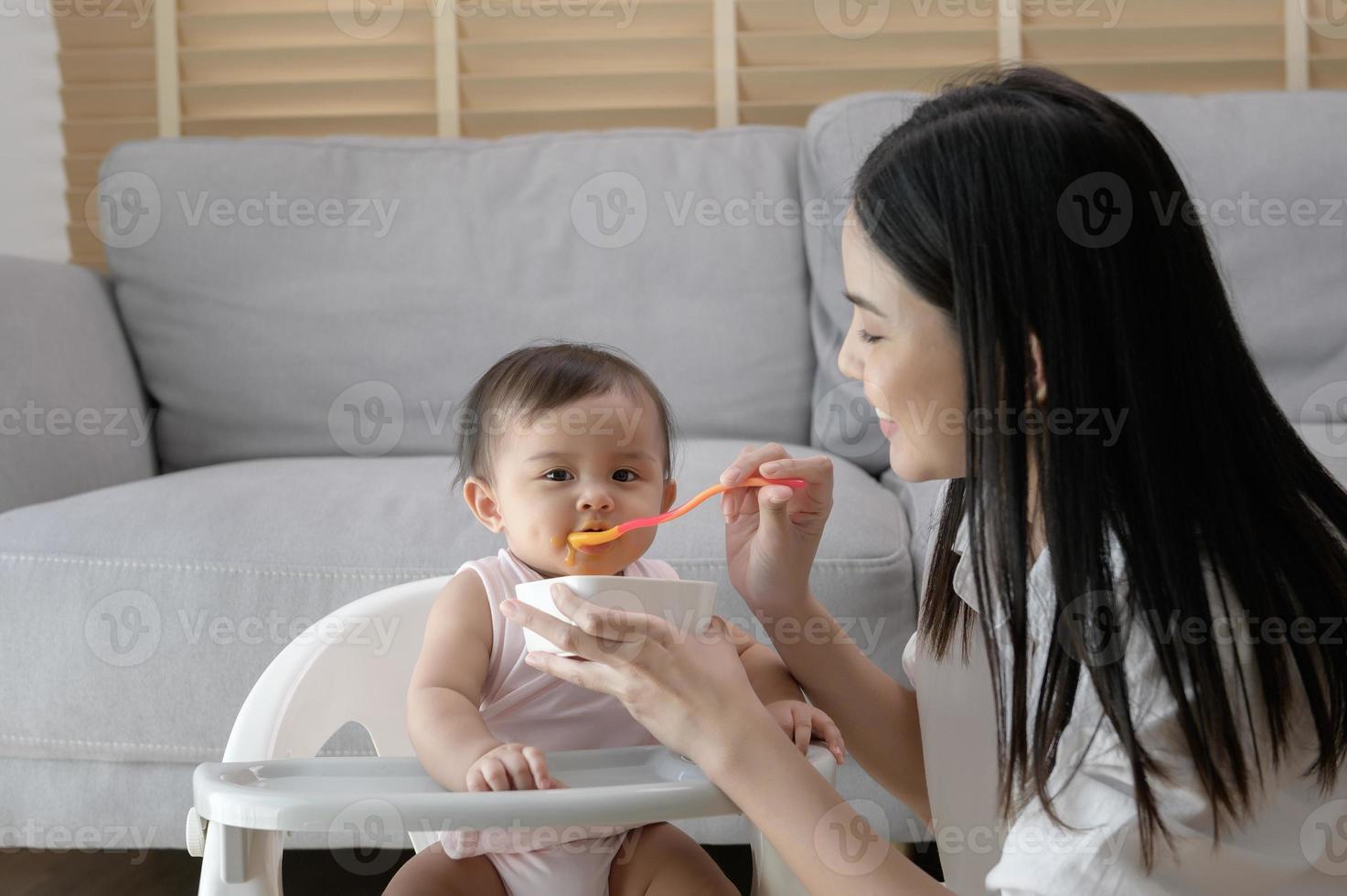 joven madre Ayudar bebé comiendo mezcla comida en bebé silla foto