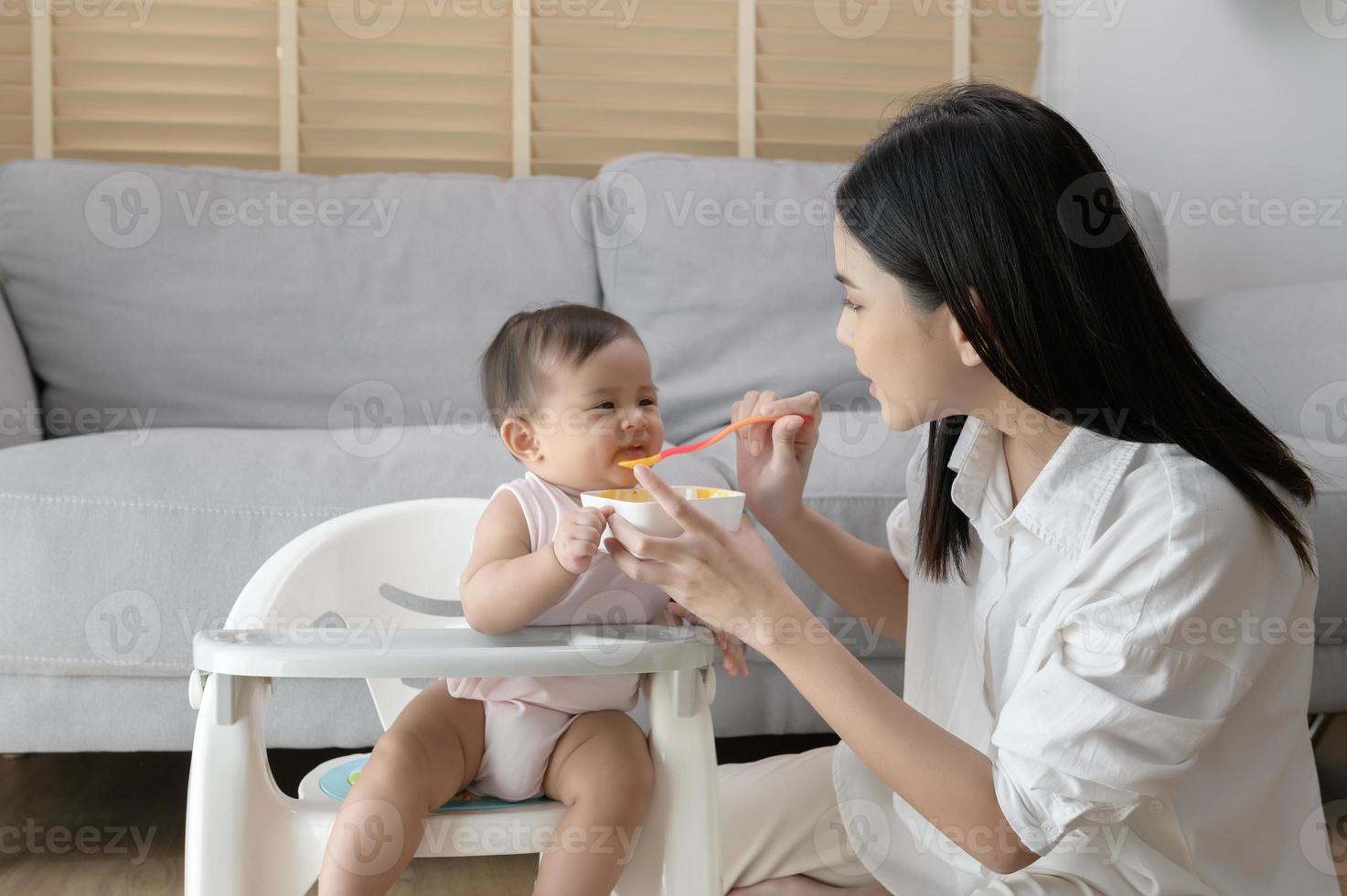 Young mother helping baby eating blend food on baby chair photo