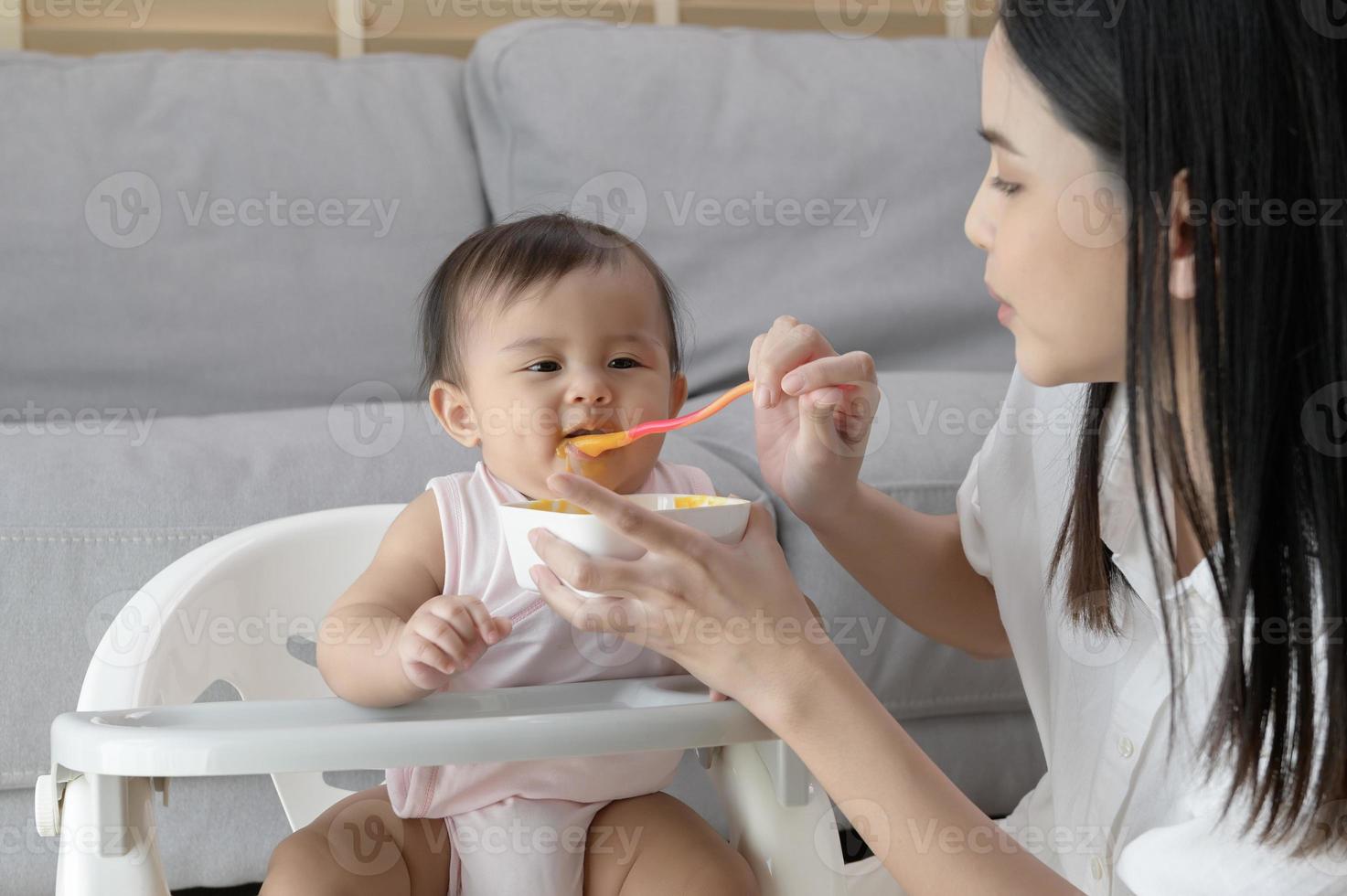 Young mother helping baby eating blend food on baby chair photo