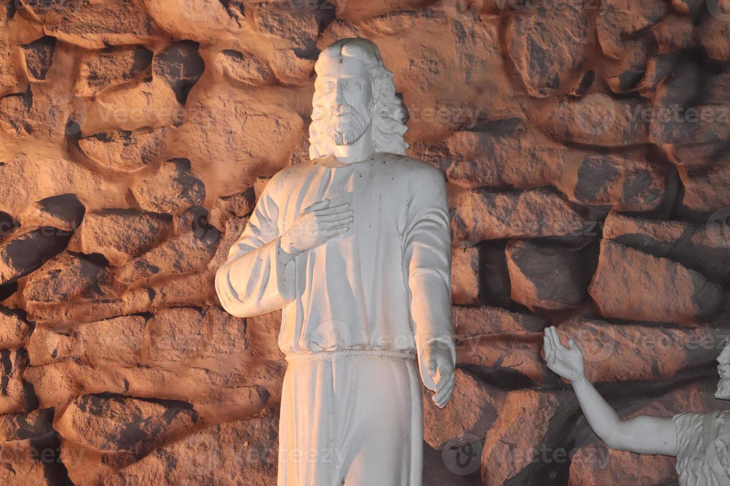 Statue of lord Jesus standing with a background of rocks fixed in the wall photo