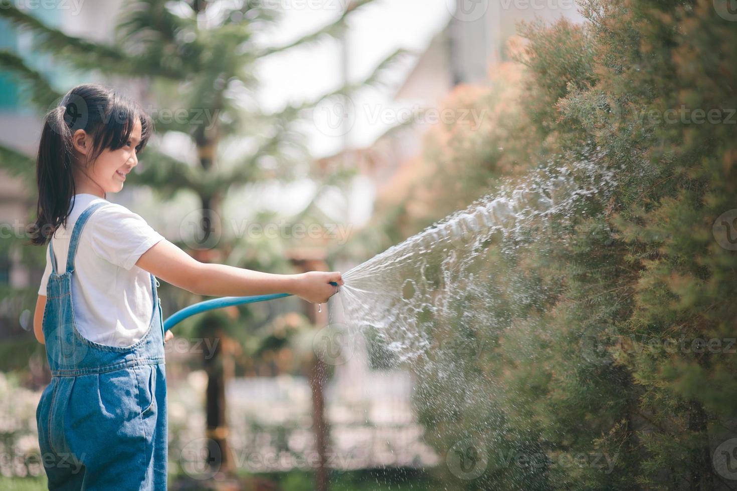 asiático pequeño niño niña agua el plantas. niño ayuda a cuidado para el plantas en el jardín. foto