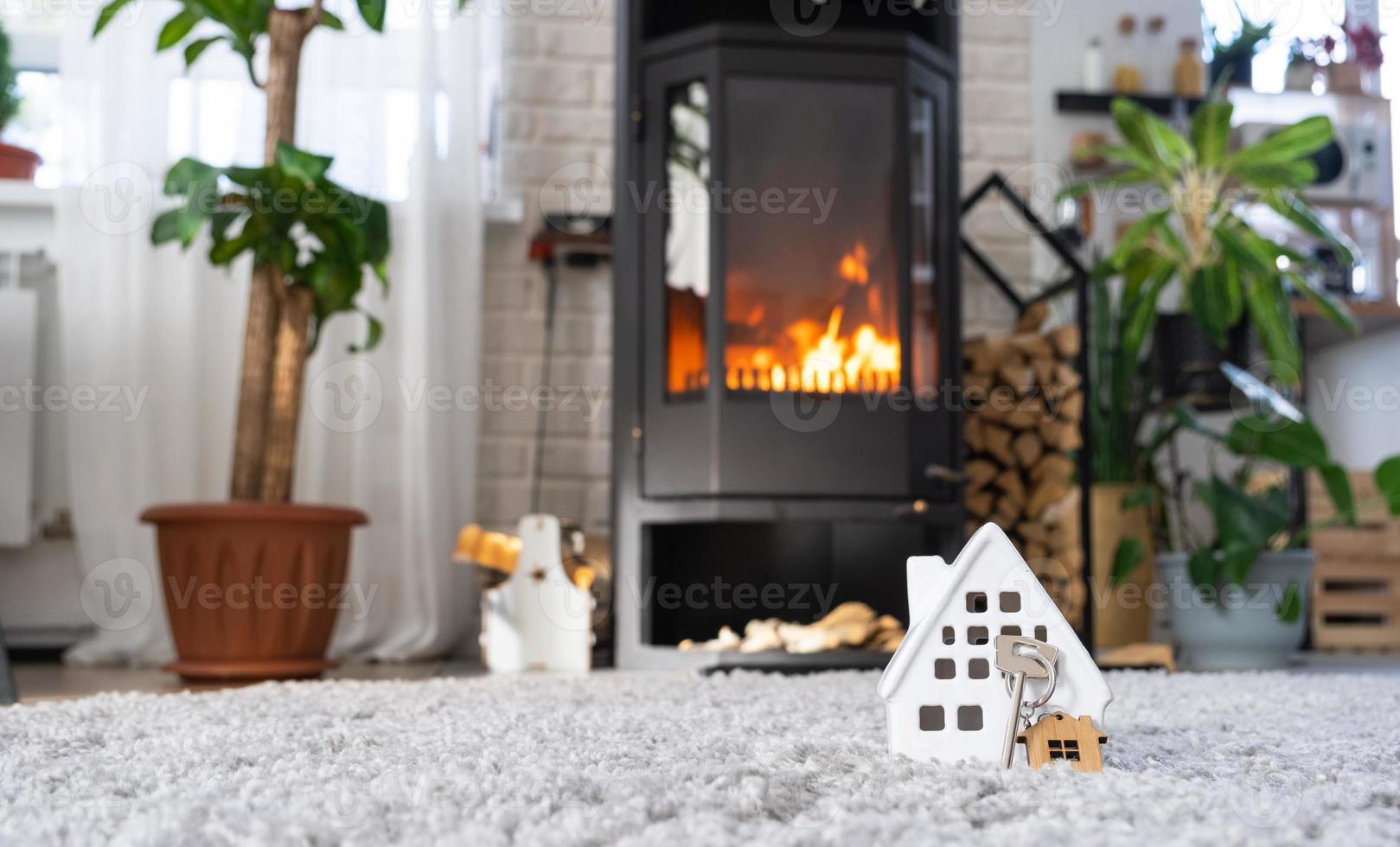 Key to house with keychain against background of fireplace stove with fire and firewood. Cozy home hearth. Building, design, project, moving to new house, mortgage, rent and purchase real estate photo