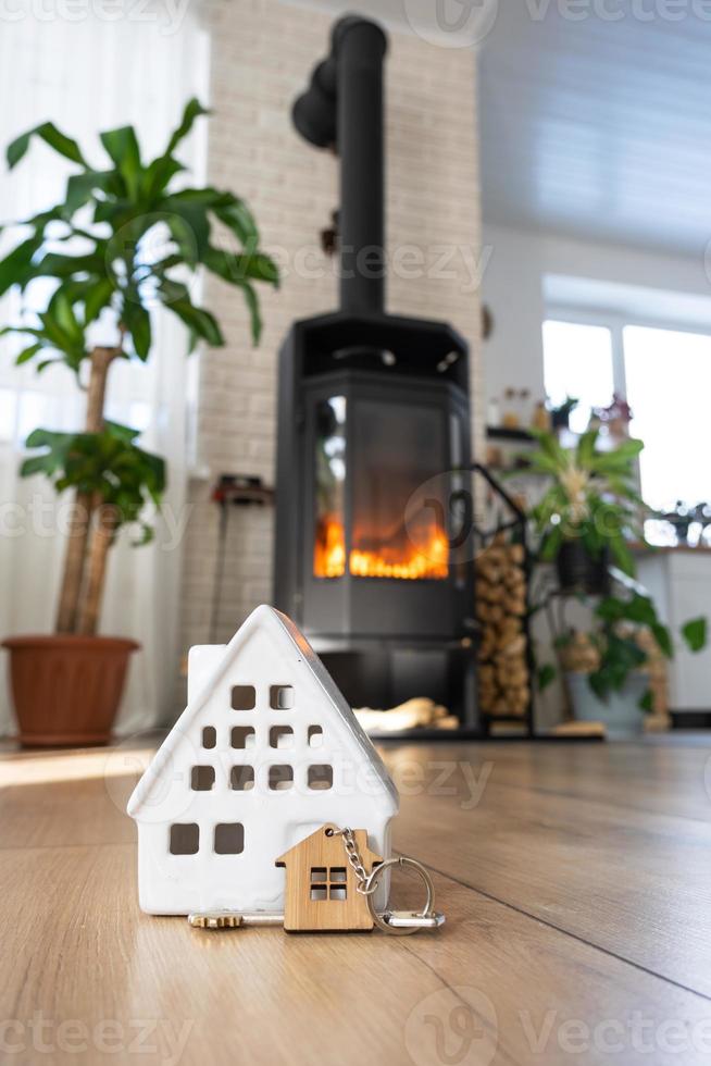 llave de casa con llavero contra el fondo de la estufa de chimenea con fuego y leña. acogedor hogar hogareño. construcción, diseño, proyecto, mudanza a casa nueva, hipoteca, alquiler y compra de bienes raíces foto