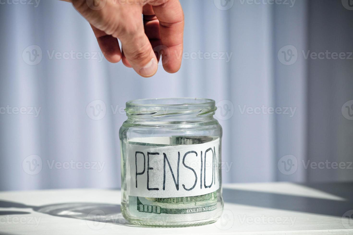 A male hand reaches into a glass jar with dollars with the text pension. photo