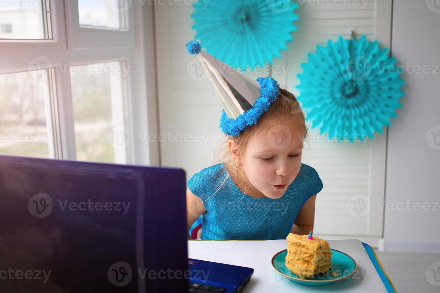 pequeño niña golpes fuera un vela en un pastel. celebrando cumpleaños vía Internet en cuarentena tiempo, autoaislamiento foto
