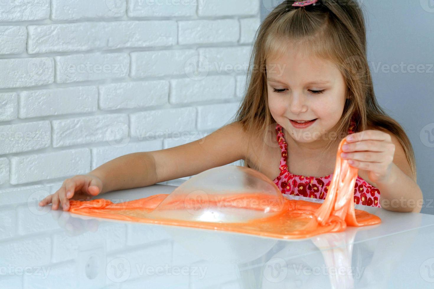 Girl playing hand made toy called slime. Children play with big orange slime. photo